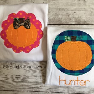 May include: Two white t-shirts with orange pumpkin appliqu&eacute;s. One pumpkin is inside a pink scalloped border with a leopard print bow. The other pumpkin is inside a blue and green plaid circle with the name "Hunter" embroidered below.
