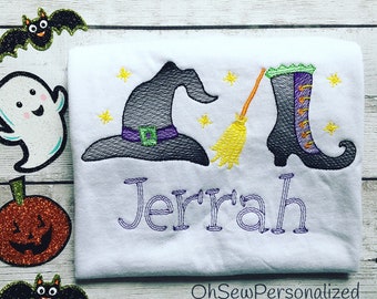 May include: White t-shirt with a Halloween-themed embroidered design. The design includes a witch hat, broom, and boot, with the name "Jerrah" embroidered in purple. Yellow stars are scattered around the design.