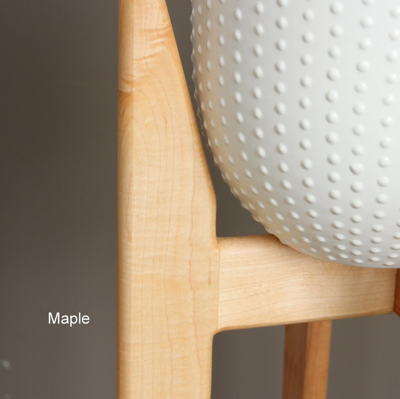 May include: A close-up of a light-colored wooden frame supporting a white, textured sphere. The wood is labeled "Maple". The sphere has a pattern of small, evenly spaced bumps across its surface. The background is a neutral gray.