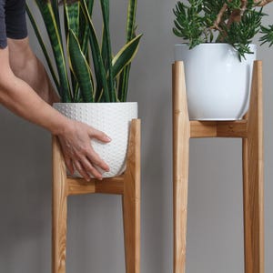 May include: Two wooden plant stands with white ceramic pots and plants. The stands are made of natural wood and have a simple, modern design.
