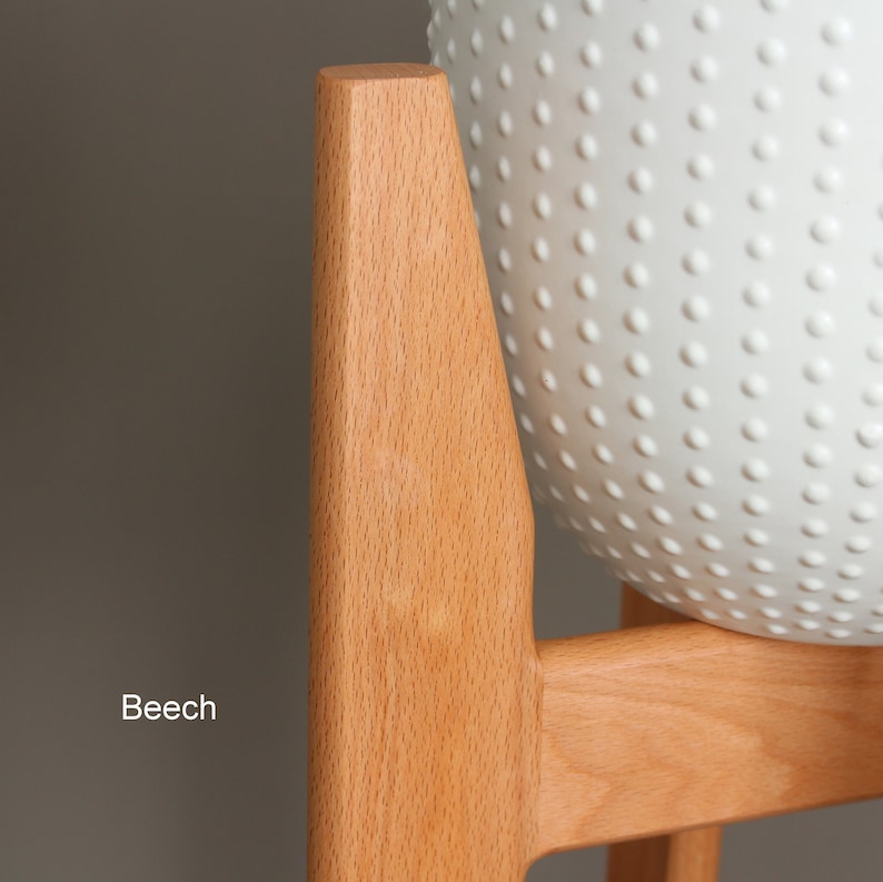 May include: A light-colored wooden plant stand with a white, textured, spherical planter. The stand is made of beech wood and has a simple, modern design. The planter has a pattern of small, raised dots.