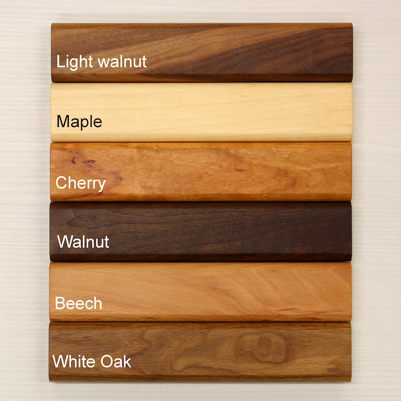 May include: A selection of wooden planks in various shades, including light walnut, maple, cherry, walnut, beech, and white oak. Each plank is labeled with its wood type. The planks are arranged horizontally, showcasing the natural grain and color variations.