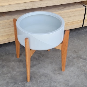 Pode incluir: Um vaso de flores azul claro com um design geom&eacute;trico, suportado por um suporte de madeira. O vaso &eacute; redondo e feito de um material dur&aacute;vel. O suporte de madeira tem quatro pernas e proporciona estabilidade. Di&acirc;metro do vaso de cerca de 30 cm.