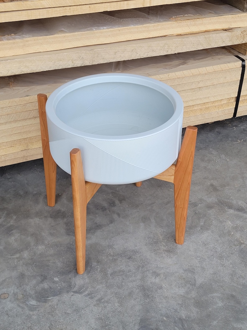 Pode incluir: Um vaso de flores azul claro com um design geom&eacute;trico, suportado por um suporte de madeira. O vaso &eacute; redondo e feito de um material dur&aacute;vel. O suporte de madeira tem quatro pernas e proporciona estabilidade. Di&acirc;metro do vaso de cerca de 30 cm.