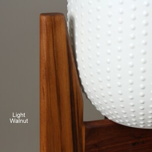 May include: A light walnut wooden plant stand with a white, textured, spherical planter. The planter has a pattern of small, evenly spaced, raised dots. The text "Light Walnut" is visible on the left side of the image.