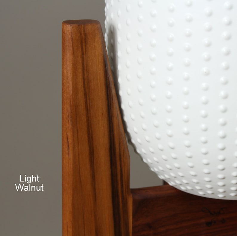 May include: A light walnut wooden plant stand with a white, textured, spherical planter. The planter has a pattern of small, evenly spaced, raised dots. The text "Light Walnut" is visible on the left side of the image.