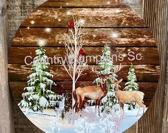 May include: A round wooden sign with a winter scene featuring two deer, a snowy forest, and red cardinals. The sign has the text "Country Pumpkins Sc" on it.