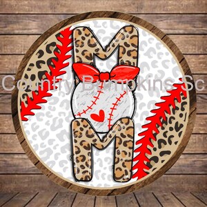 May include: A round wooden sign with a white background and a red and white baseball design. The letters "MOM" are in the center of the sign, with a baseball in the middle of the "O". The letters are covered in a leopard print pattern.