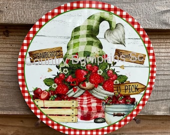 May include: A round metal sign with a red and white checkered border. The center of the sign features a gnome wearing a green and white checkered hat and holding a basket of strawberries. The sign also includes the text "Strawberries", "50 cents per qt", and "U Pick".