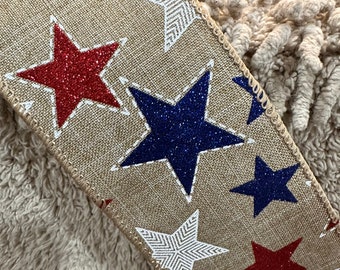 May include: A burlap ribbon with a repeating pattern of red, white and blue stars. The stars are outlined in white and have a glittery finish.
