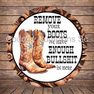 May include: Round sign with a brown leather-like border and a white center. The center features two brown cowboy boots and the text "REMOVE your BOOTS We have ENOUGH BULLSHIT IN HERE."