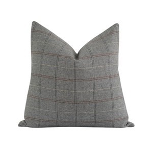 Puede incluir: Un coj&iacute;n decorativo cuadrado con un estampado de cuadros grises. El coj&iacute;n tiene una combinaci&oacute;n de colores neutros con un dise&ntilde;o de cuadr&iacute;cula en tonos de gris, marr&oacute;n y blanquecino. El coj&iacute;n est&aacute; hecho de una tela suave y texturizada.
