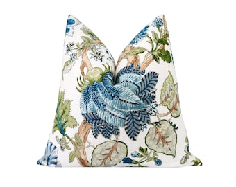 May include: A white pillow with a blue and green floral pattern. The pillow features a large blue flower with green leaves and branches.