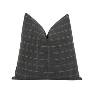 May include: A gray decorative pillow with a plaid pattern. The pillow features a grid design with white and gold lines. The pillow is square-shaped and has a soft, textured appearance.