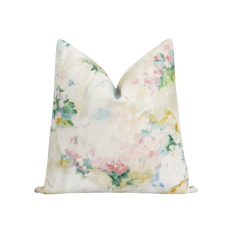 K&ouml;nnte beinhalten: Ein quadratisches Zierkissen mit einem Aquarell-Blumenmuster. Der cremefarbene Hintergrund ist mit sanften Pinselstrichen in Rosa, Gr&uuml;n, Gelb und Blau verziert. Das Design erzeugt eine sanfte, k&uuml;nstlerische &Auml;sthetik f&uuml;r die Inneneinrichtung.
