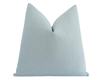 Könnte beinhalten: Ein quadratisches Dekokissen in einfarbigem Hellblau. Der Stoff weist eine subtile, feinkörnige vertikale Textur auf der gesamten Oberfläche auf. Das Kissen ist oben mittig eingedrückt, wodurch zwei Spitzen und eine weiche Faltung entstehen.