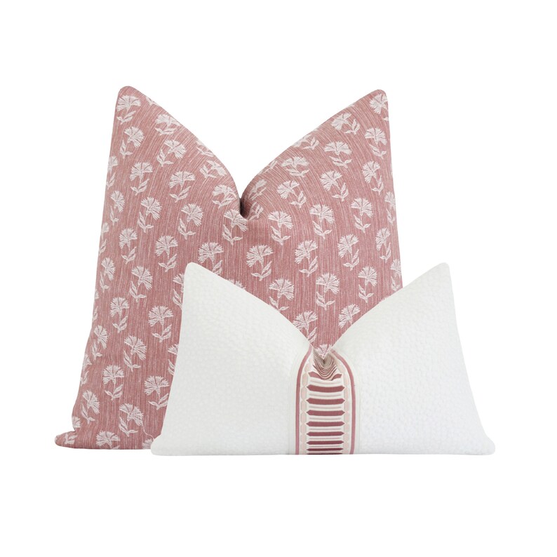 May include: Two decorative throw pillows. One is a dusty rose color with a white floral pattern. The other is white with a textured surface and a vertical stripe of dusty rose and white detail.