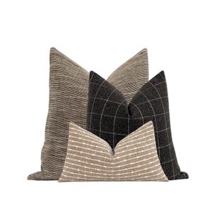 May include: Three decorative throw pillows in a neutral color palette. The largest pillow is a natural linen with a subtle texture. The middle pillow is a black and white plaid. The smallest pillow is a natural linen with a white stripe pattern.