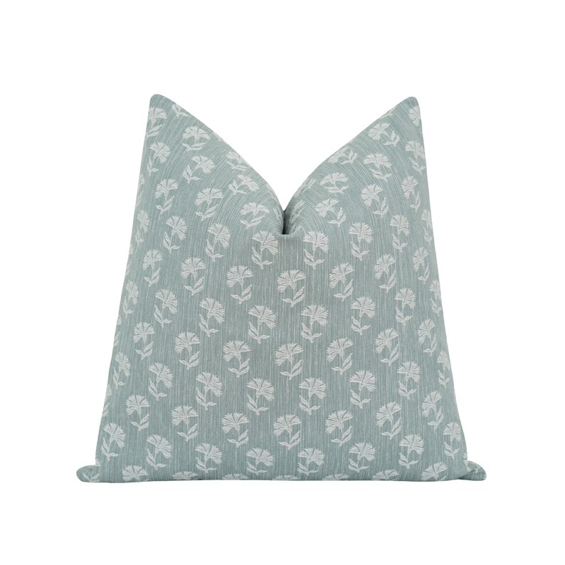 May include: A square decorative pillow with a light teal background and a repeating white floral pattern. The pillow has a textured appearance and a soft, inviting look, perfect for adding a touch of elegance to any living space.