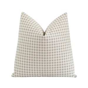 May include: A square throw pillow featuring a classic gingham pattern in light beige and white. The fabric displays a consistent checkered grid design across the entire surface, with a soft, plump shape and a distinct crease at the top center.