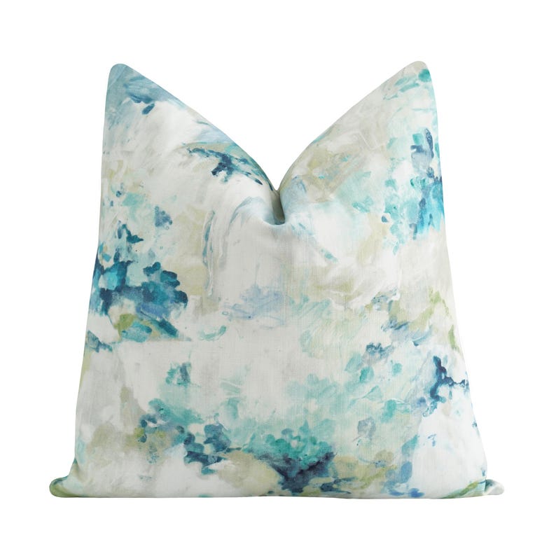 K&ouml;nnte beinhalten: Ein quadratisches Zierkissen mit einem Aquarelldesign. Das Kissen hat einen wei&szlig;en Hintergrund mit blauen, t&uuml;rkisfarbenen und gr&uuml;nen Pinselstrichen. Das Kissen hat ein weiches, strukturiertes Aussehen.