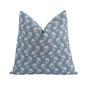 May include: A square decorative pillow with a blue background and a white floral pattern. The pillow has a textured appearance and is designed for home decor.
