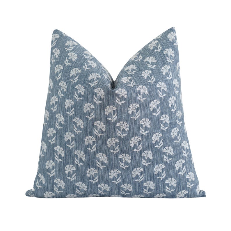 May include: A square decorative pillow with a blue background and a white floral pattern. The pillow has a textured appearance and is designed for home decor.