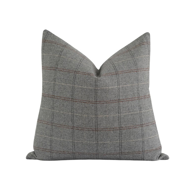 Puede incluir: Un coj&iacute;n decorativo cuadrado con un estampado de cuadros grises. El coj&iacute;n tiene una combinaci&oacute;n de colores neutros con un dise&ntilde;o de cuadr&iacute;cula en tonos de gris, marr&oacute;n y blanquecino. El coj&iacute;n est&aacute; hecho de una tela suave y texturizada.