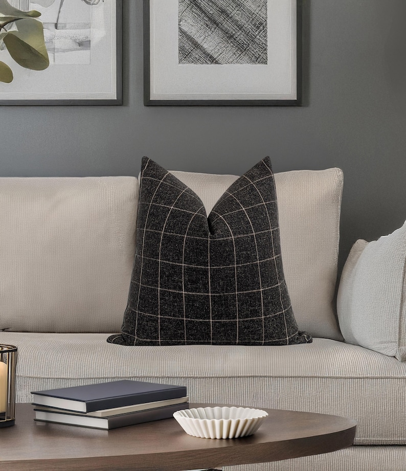 May include: A black and white plaid throw pillow with a subtle brown stripe on a light beige couch.