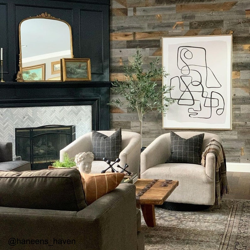 May include: A living room interior with a black fireplace, a white and gray patterned rug, two white armchairs with black and white plaid cushions, a wooden coffee table, and a large abstract art print on the wall. The art print features a black line drawing of geometric shapes on a light gray background.