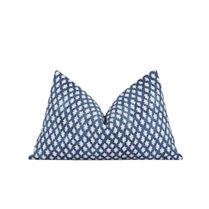 Op de afbeelding: Een decoratief sierkussen met een blauw-wit geometrisch patroon. Het kussen heeft een donkerblauwe achtergrond met een herhalend wit bloemmotief. Het is rechthoekig en heeft een zacht, getextureerd uiterlijk.