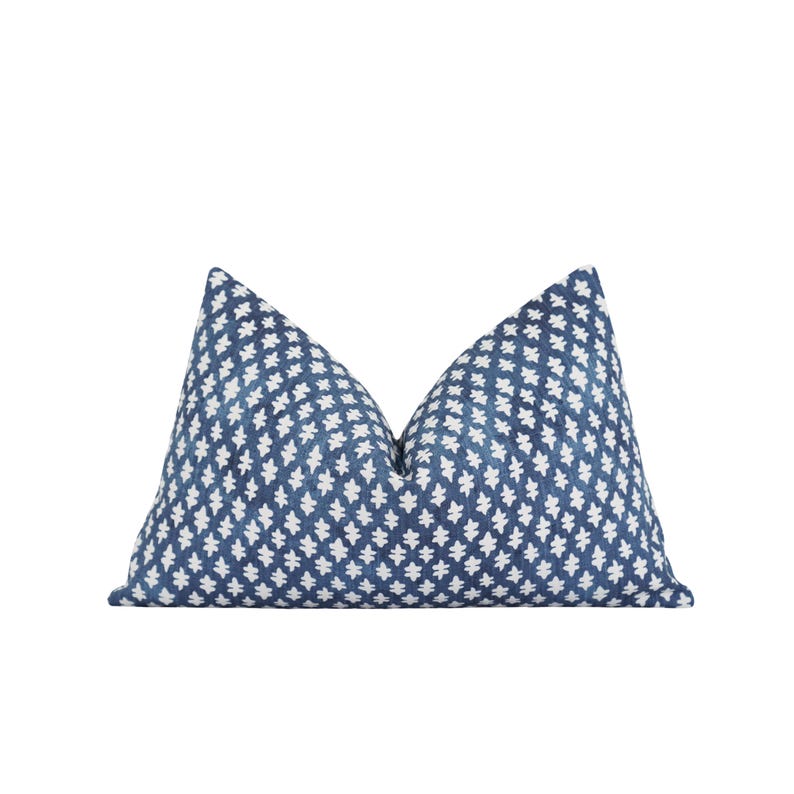 Op de afbeelding: Een decoratief sierkussen met een blauw-wit geometrisch patroon. Het kussen heeft een donkerblauwe achtergrond met een herhalend wit bloemmotief. Het is rechthoekig en heeft een zacht, getextureerd uiterlijk.