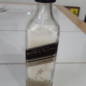 May include: A clear glass bottle of Johnnie Walker Double Black whisky, filled with a white liquid. The bottle has a black and gold label with the brand name and logo. The bottle is 50 ml and 40% alc/vol.