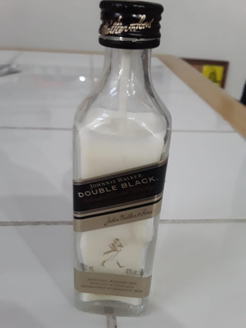 May include: A clear glass bottle of Johnnie Walker Double Black whisky, filled with a white liquid. The bottle has a black and gold label with the brand name and logo. The bottle is 50 ml and 40% alc/vol.