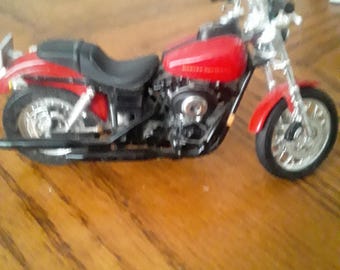 May include: A red and black toy motorcycle with chrome accents. The motorcycle has a black seat, a red gas tank with white lettering, and silver wheels. The toy is on a wooden surface.