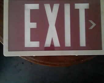 May include: Rectangular exit sign with a white border. The sign has a maroon background with the word "EXIT" in large, white capital letters. A white arrow points to the right. The sign is likely for commercial or public buildings.