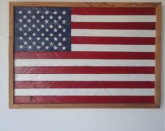 May include: A wooden American flag with red, white, and blue paint. The flag is framed in a natural wood frame.