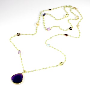 May include: A long gold chain necklace with a large purple teardrop pendant. The chain is made of small green beads and features various coloured gemstones.