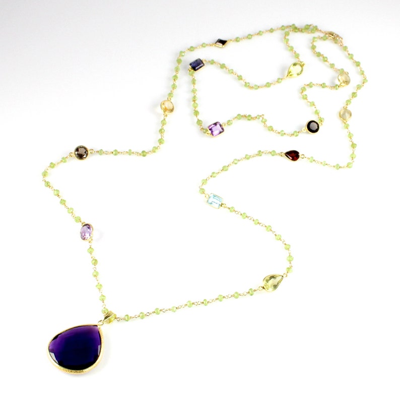 May include: A long gold chain necklace with a large purple teardrop pendant. The chain is made of small green beads and features various coloured gemstones.