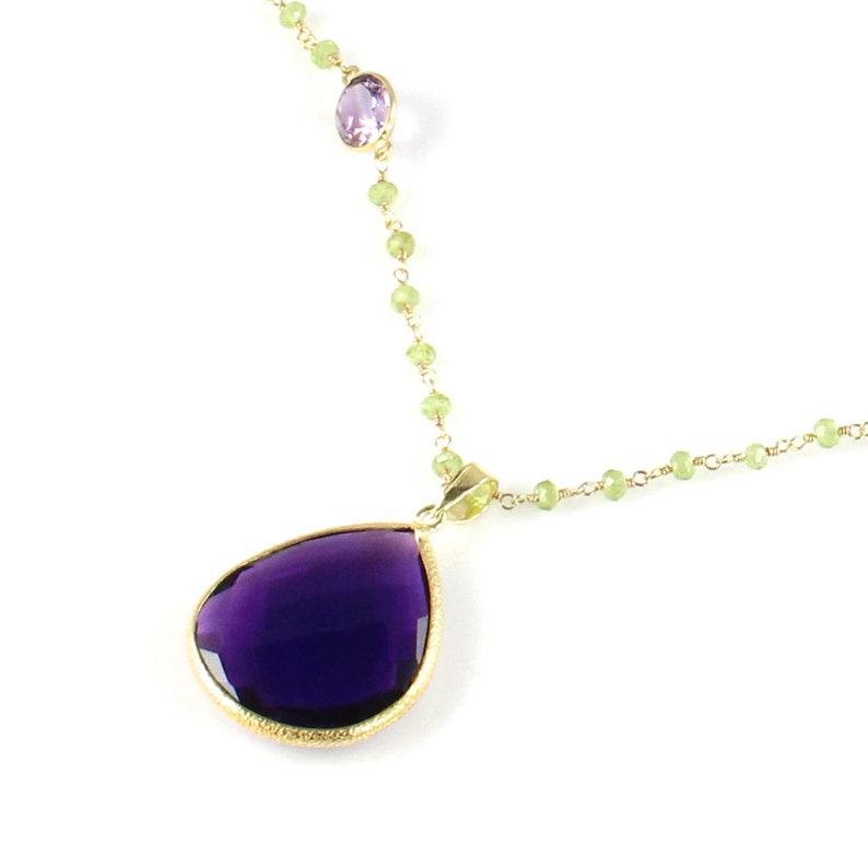 May include: A gold chain necklace with a large purple teardrop pendant and a smaller purple gemstone accent. The chain is made of small green beads.