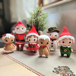 May include: A collection of crocheted Christmas decorations, including a gingerbread person, a snowman, a Father Christmas, and two elves. The decorations are all handmade and feature intricate details.