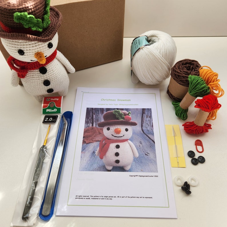 May include: A crochet Christmas snowman kit with white yarn, green, red, and orange yarn scraps, a crochet hook, a pair of tweezers, a needle, safety pins, and black and white buttons. The kit also includes a pattern for crocheting a snowman.