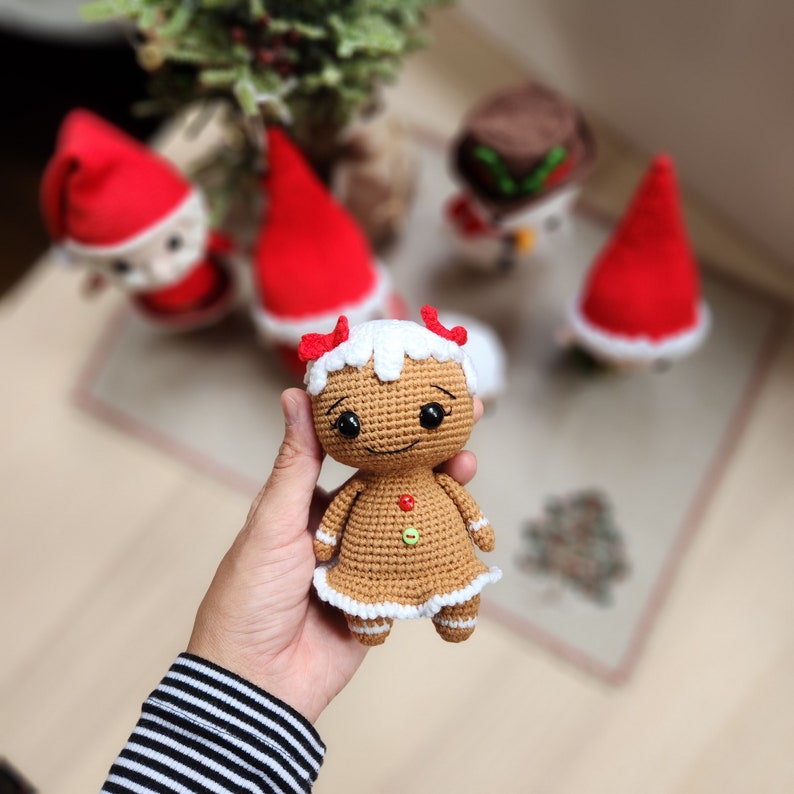 May include: A crocheted gingerbread person doll with white icing and red candy accents. The doll is holding a red candy cane in its right hand and has a friendly smile.
