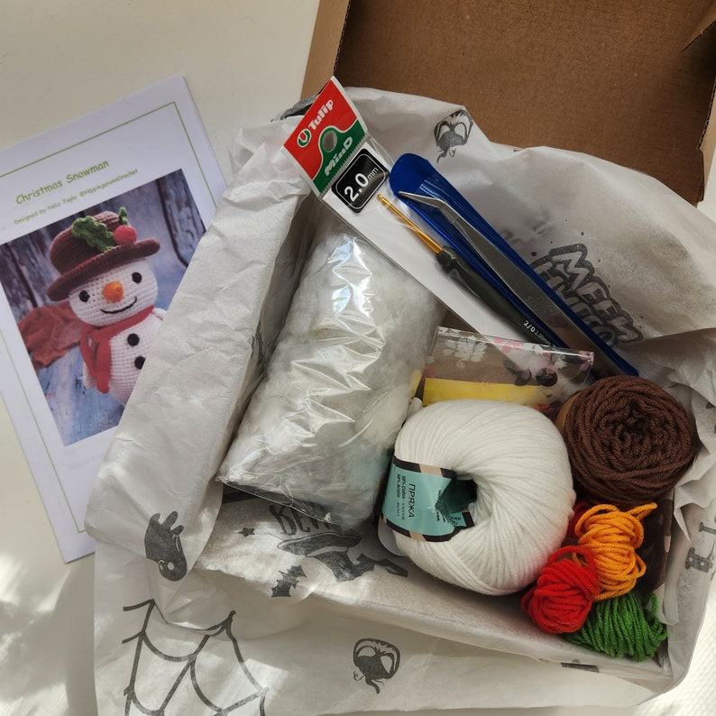 May include: A craft kit for crocheting a Christmas snowman. The kit includes white yarn, brown yarn, orange yarn, green yarn, stuffing, a crochet hook, a pair of scissors, and instructions. The kit also includes a pattern for a crocheted snowman.