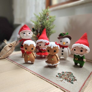 May include: A collection of crocheted Christmas decorations, featuring Santa Claus, a gingerbread person, a snowman, an elf, and a Christmas tree. The decorations are all handmade and have a charming, festive appearance.