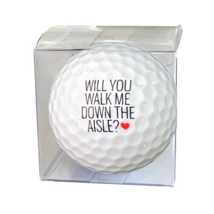 May include: A white golf ball with the text "Will you walk me down the aisle?" and a small red heart.