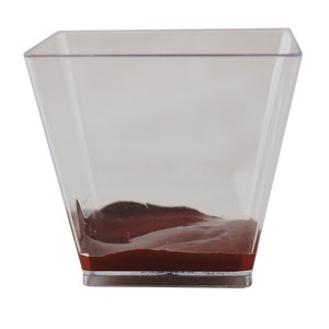 May include: A clear plastic square dish with a layer of dark brown chocolate mousse at the bottom.