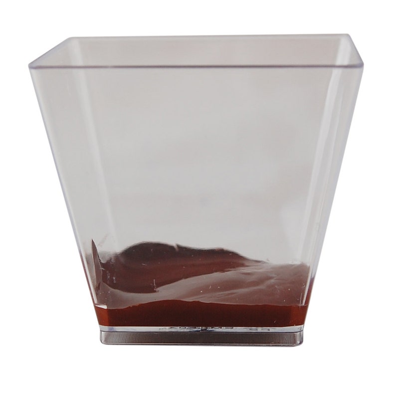 May include: A clear plastic square dish with a layer of dark brown chocolate mousse at the bottom.