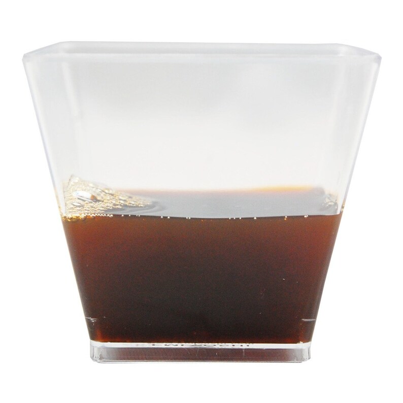 May include: A clear, square-shaped plastic cup filled with a dark brown liquid. The liquid is about halfway up the cup and has a slightly foamy surface. The cup is set against a plain white background.