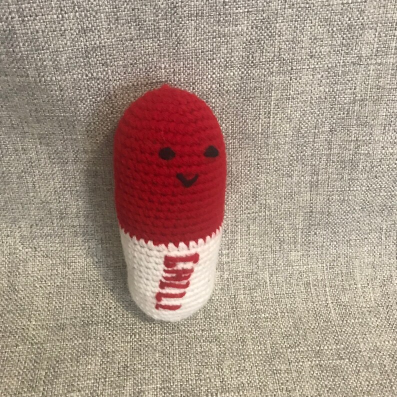 May include: A red and white crocheted pill-shaped toy with a smiling face.
